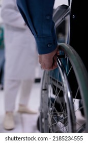 Selective Focus On Senior Man Living With Disability In Front Of Medical Doctor For Appointment In Private Hospital Reception. Closeup Of Older Man Hand Using Wheelchair At Medical Clinic.