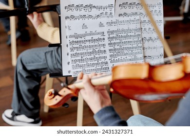 Selective focus on sheet music shot of unrecognizable students playing musical instruments in school orchestra - Powered by Shutterstock