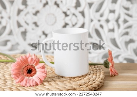 Selective focus on single one white mug mock up. Cup on home table with decorative spring flowers on background and bohemian style wood panel. Cozy seasonal products advertisement background.