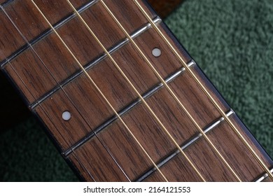 Selective focus on small twelfth fret marker dot on a walnut board. Tight focus includes sections position indicators of the steel E and A strings D and G Strings B and E Strings. 