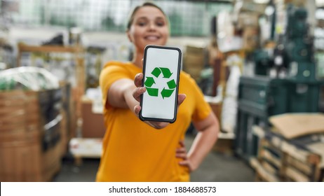 Selective focus on smartphone screen with green recycling sign in hand of happy caucasian young girl working on garbage station, widescreen. Waste sorting and recycling concept - Powered by Shutterstock