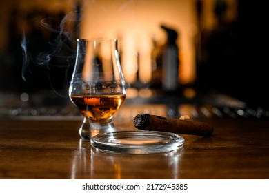 Selective Focus On Smoking Cigar On Ashtray And Glass With Whiskey On Blurred Bar Background