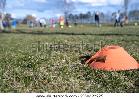 Selective focus on a soccer practice field cone on grass with blurred kids in the background