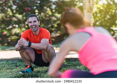 Selective Focus On A Squatting Smiling Man Exercising In A Park With Other People In A Personal Training Session.