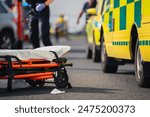 Selective focus on stretcher against ambulance cars of emergency medical service, firefighters and rescue helicopter on road. Themes rescue, urgency and health care.	
