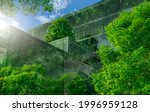 Selective focus on tree and eco friendly building with vertical garden in modern city. Green tree forest on sustainable glass building. Office building with green environment. Go green concept.