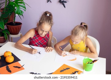 selective focus two Cute schoolgirls  they are sitting at table   drawing Halloween symbols paper and pencils  making decorations for the holiday