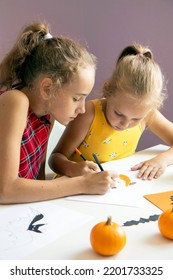 selective focus two schoolgirls  they are sitting at table   drawing Halloween symbols paper and pencils  making decorations for the holiday  The concept children's crafts   drawings