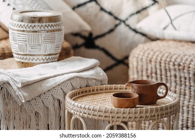 Selective focus on two wooden cup standing at bamboo coffee table in bright and cozy living room with blurred background. Wicker furniture with eco materials, candle and textile at boho chic interior
