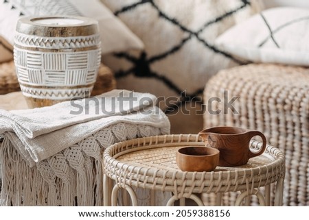 Selective focus on two wooden cup standing at bamboo coffee table in bright and cozy living room with blurred background. Wicker furniture with eco materials, candle and textile at boho chic interior