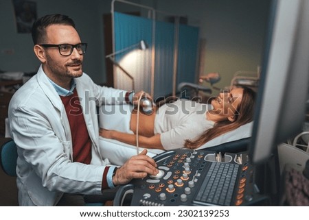 Selective focus on ultrasound scanner device in the hand of a professional doctor examining his patient doing abdominal ultrasound scanning sonogram sonography sonographer early pregnancy