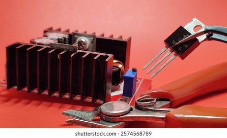 Selective focus on various shaped electronic components and repair equipment with a dark red background and a blurred image of a black electronic circuit board.