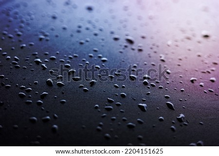 Selective focus on water drops on slippy surface of black synthetic fabric with bright light from background.
