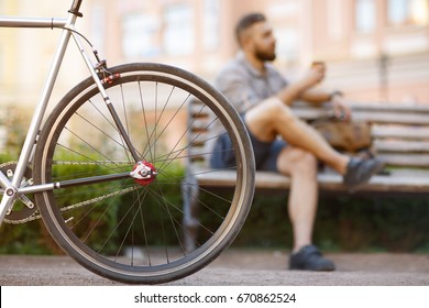 Selective Focus On A Wheel Of A Bicycle Copyspace Urban Male Rider Relaxing On The Bench Having Coffee On The Background Cycling Cyclist Lifestyle Transport Ecology Hipster Travel Outdoors Active