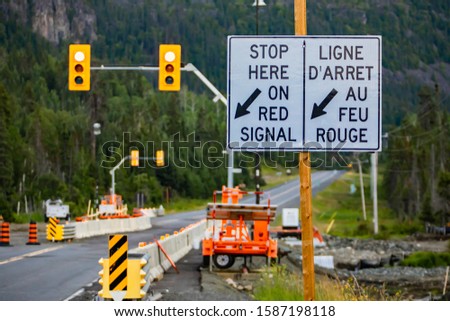selective focus on a white road sign on Wooden pole, road work zone with Machines in the background, stop here on red signal, with arrow
