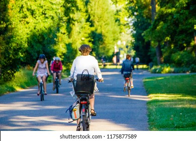 Selective Focus On A Woman Cycling On Her Bike With Many Other In The Background On A Sunny Summer Day. Driving To Work Or School With The Bike To Have A Healthy Lifestyle