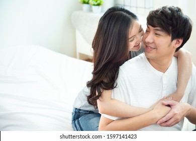 Selective Focus On Woman Face With Portrait Of Young Asian Couple Girl Piggyback Man From Back On Bed,romantic Asia People In Love Hugging While Sitting In Bed,valentine Day Concept With Copy Space.