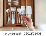 Selective focus on woman hand holding stainless steel spoon against blurred cutlery set in wooden organizer. Tidyness and neat in kitchen drawer. Keeping silverware clean concept