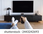 Selective focus on woman hand hold remote control and turn on tv panel on wall while relaxing on comfort sofa in living room. POV female choosing channel for watching television at home