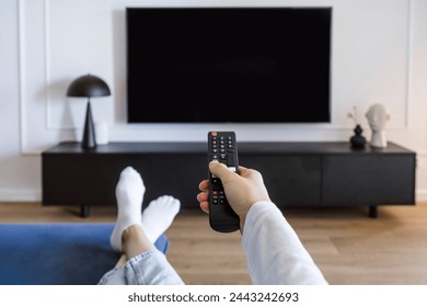 Selective focus on woman hand hold remote control and turn on tv panel on wall while relaxing on comfort sofa in living room. POV female choosing channel for watching television at home - Powered by Shutterstock