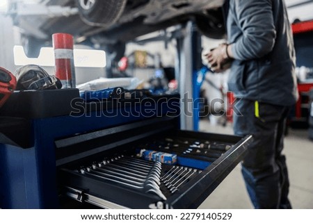 Selective focus on a wrenches and tools in a drawer on a mechanic toolbox with a worker fixing car in a blurry background at workshop.