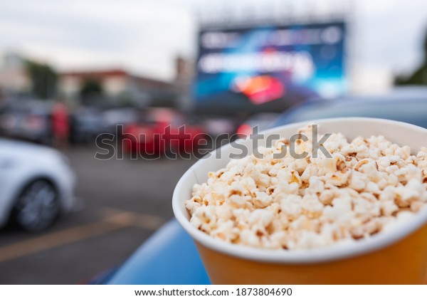 Selective focus on yellow bucket full of popcorn\
on car parking at drive-in cinema background. Free time, leisure\
and entertainment\
concept