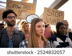 Selective focus on young blonde woman with group of diverse people protesting against war in silence with serious gesture. Different activists with anti-war banners at demonstration for peace outdoors