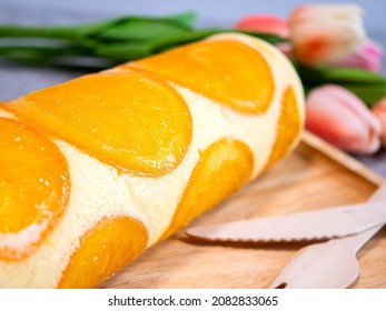 Selective focus of orange cake roll with slice orange fruit on wooden plate.