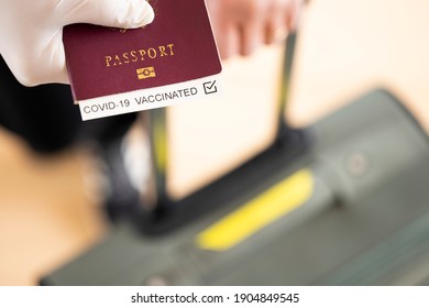 (Selective focus) Overhead view of an human hand wearing a latex glove, holding a passport with 'Covid-19 Vaccinated' label inside it. Travel concept during the Covid-19 pandemic.