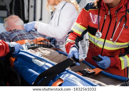 Selective focus of paramedic holding belts of stretcher near patient and colleagues outdoors