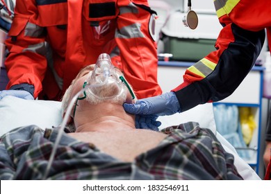 Selective focus of paramedic in latex glove checking pulse of senior patient in oxygen mask near colleague during first aid - Powered by Shutterstock