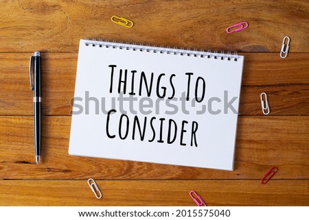 Selective focus of a pen, paper clips and notebook written with Things To Consider on wooden background.