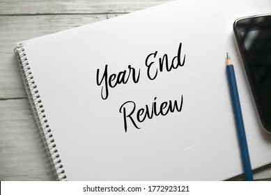 Selective Focus Of Pencil,mobile Phone And Notebook Written With Year End Review On White Wooden Background.