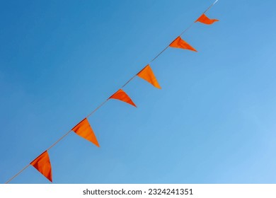 Selective focus of pennant orange flags waving in the air with blue clear sky as background, Orange colour fever is a phenomenon in the Netherlands that occurs during major events in Dutch culture. - Powered by Shutterstock