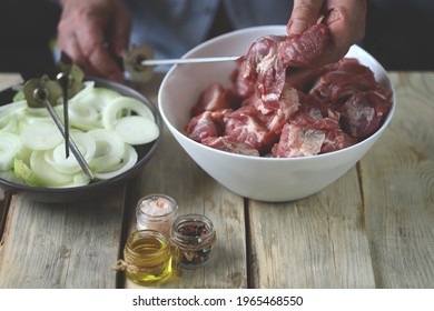 Selective focus. Pieces of raw meat for barbecue and onion rings in a bowl. Hands stir the marinated meat. - Powered by Shutterstock