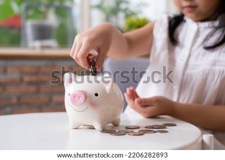 Selective focus at piggy bank while young girl putting coin in to it for her personal saving. Saving money concept of young kids ideal for education or personal saving plan since young age.