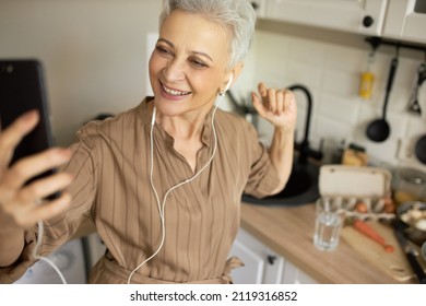 Selective Focus Of Pretty Mature Caucasian Woman In White Earphones Doing Selfie At Kitchen While Cooking Breakfast, Smiling, Having Fun, Getting Ready To Go For Work. Human Emotions And Feelings