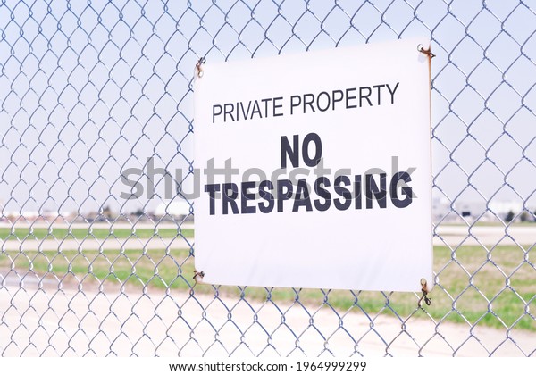 Selective focus of Private\
Property No Trespassing sign board on metal mesh net fence with\
blurred field.
