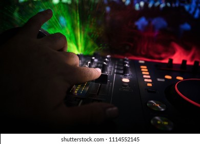 In selective focus of Pro dj controller.The DJ console deejay mixing desk at music party in nightclub with colored disco lights. Close up view