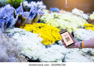 Selective focus to QR Code tag on smart phone in hand of customer with blurry many flowers in flower shop at Bangkok flower market, Thailand. Qr code payment concept.