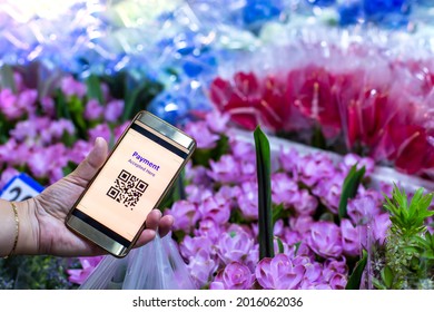 Selective focus to QR Code tag on smart phone in hand of customer with blurry many flowers in flower shop at Bangkok flower market, Thailand. Qr code payment concept.
