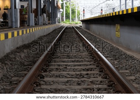 Selective focus of railway tracks at a train station in Yogyakarta, Indonesia, creating a strong perspective line toward the distance. The photo highlights the industrial texture of steel rails, gravel stones, and urban transportation infrastructure with a dramatic and minimalist composition. Perfect for themes related to travel, transportation, railway industry, commuting, journey concepts, engineering, and urban development.