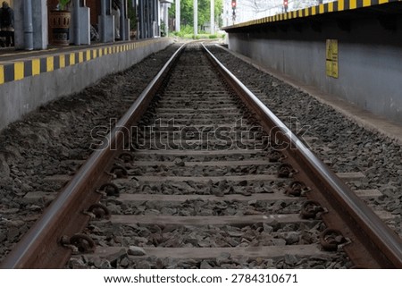 Selective focus of railway tracks at a train station in Yogyakarta, Indonesia, creating a strong perspective line toward the distance. The photo highlights the industrial texture of steel rails, gravel stones, and urban transportation infrastructure with a dramatic and minimalist composition. Perfect for themes related to travel, transportation, railway industry, commuting, journey concepts, engineering, and urban development.