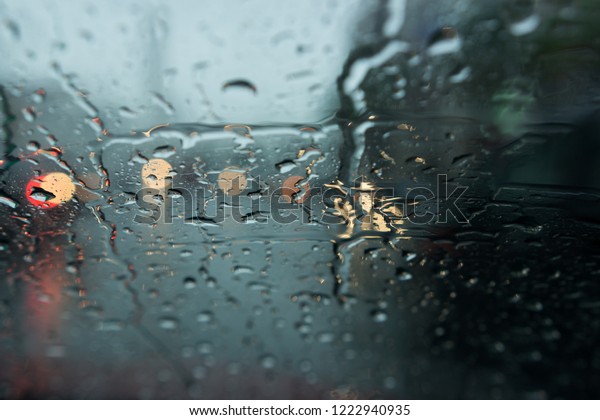 Selective focus of rain drop on car wind\
shield. Road view through car window blurry with heavy rain,\
Concept of driving in rain, bad driving\
conditions.
