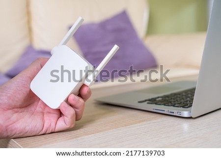 Selective focus at range extender. Internet router on working table with blurred man connect the cable at the background. Fast and high speed internet connection to cover home network usage.