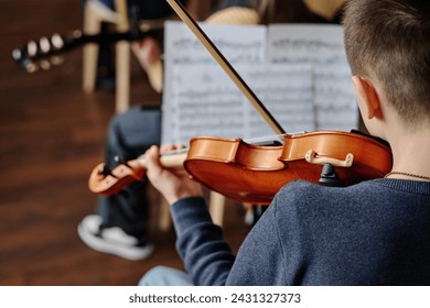 Selective focus rear view shot of unrecognizable teen boy playing violin in school orchestra, copy space - Powered by Shutterstock