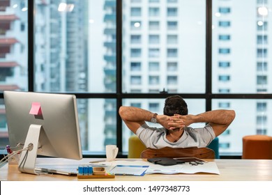 Selective focus rear view young businessman sitting at work desk and napping on the chair in office building. Relax young smart manager business man taking break resting at modern office workplace.