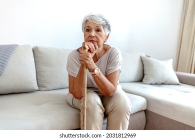 Selective focus of a retired woman with her wooden walking stick at home. Cropped shot of a senior woman using a walking stick at home. Old gray hair Serious lady supporting on a walking cane at home. - Powered by Shutterstock