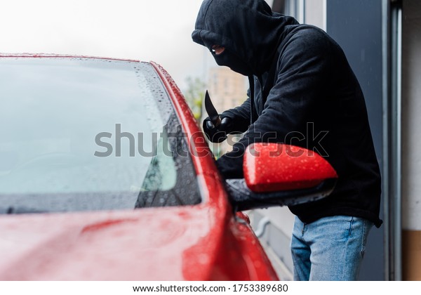 Selective focus of robber in balaclava holding\
knife near car on urban\
street