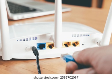 Selective focus at router antenna while men hand connecting fiber cable plug into socket with blurred computer laptop at the background. High speed broadband internet technology at home concept.
